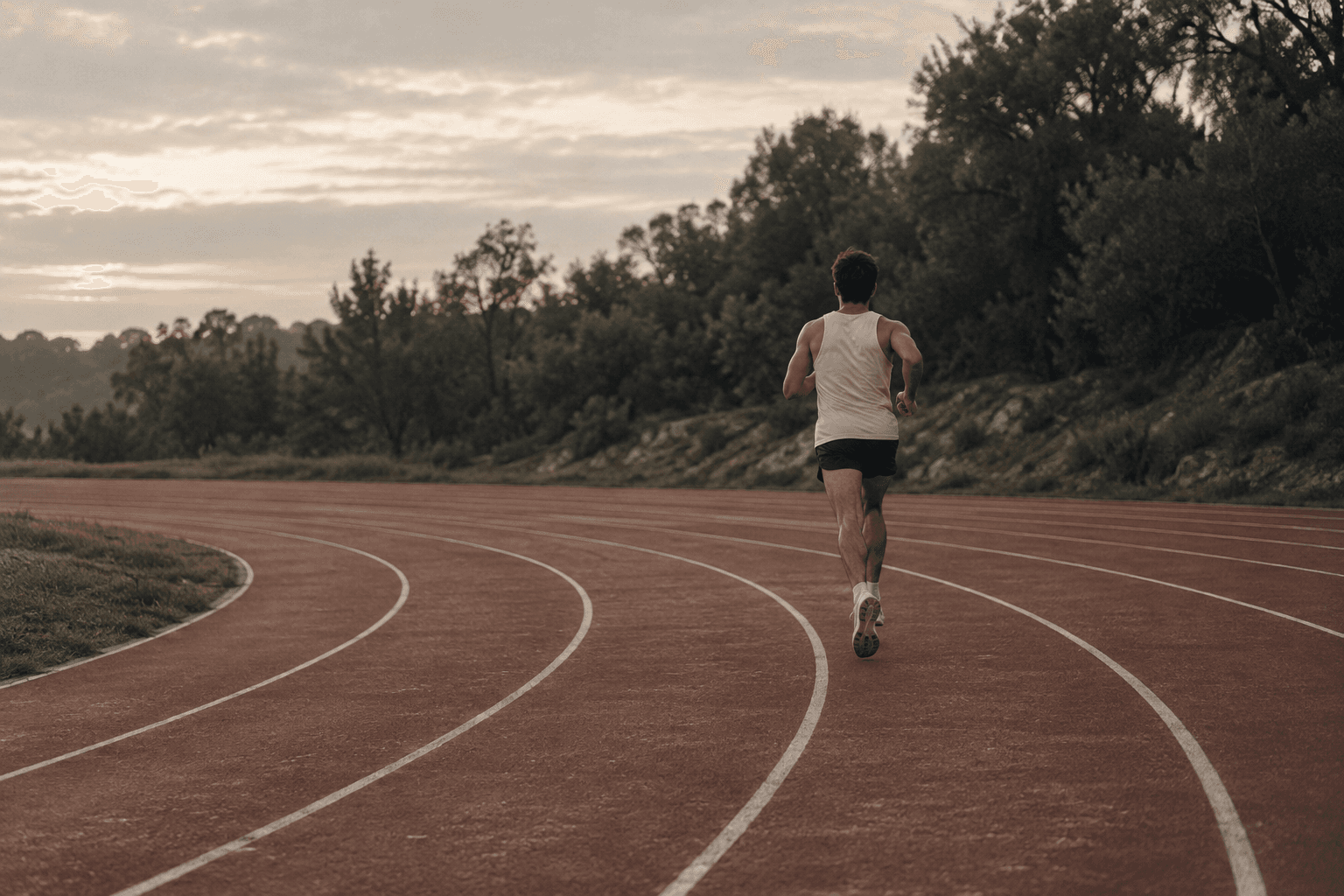 A runner following the curve of a quiet athletics track in soft morning light.